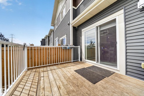 Spacious wood-finish deck with white railings and a privacy fence, featuring a sliding glass door entry to the interior - 1099 Eaton Road, Edmonton, AB 