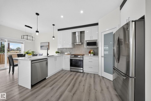 Modern kitchen featuring white cabinetry, stainless steel appliances, and wood-finish flooring - 1099 Eaton Road, Edmonton, AB 