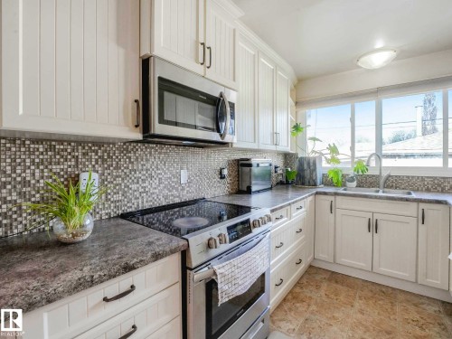 Kitchen featuring white cabinetry, mosaic tile backsplash, solid surface countertops, and a stainless steel over-the-range microwave - 9207 169 Street, Edmonton, AB - Indoor Photo Showing Kitchen With Double Sink With Upgraded Kitchen