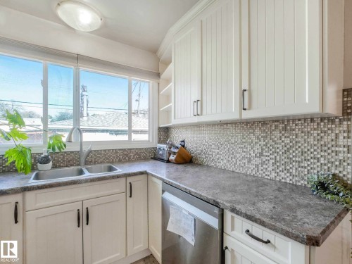 Kitchen featuring a double basin stainless steel sink, a large window, white shaker-style cabinetry, mosaic tile backsplash, and a stainless steel dishwasher - 9207 169 Street, Edmonton, AB - Indoor Photo Showing Kitchen With Double Sink