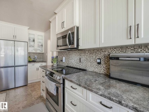 Kitchen featuring white cabinetry, mosaic tile backsplash, stainless steel appliances, and stone-finish countertops - 9207 169 Street, Edmonton, AB - Indoor Photo Showing Kitchen With Upgraded Kitchen