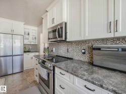 Kitchen featuring white cabinetry, mosaic tile backsplash, stainless steel appliances, and stone-finish countertops - 