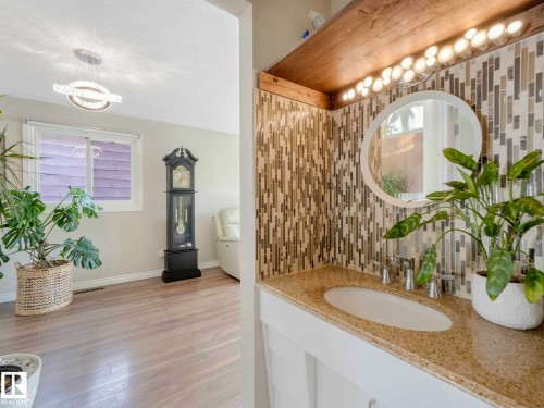 Vanity featuring a mosaic tile backsplash, granite-finish countertop with an undermount sink, and a circular mirror - 9207 169 Street, Edmonton, AB - Indoor Photo Showing Bathroom