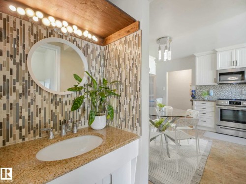 Vanity featuring a mosaic tile backsplash, oval mirror, and a countertop with an integrated sink - 9207 169 Street, Edmonton, AB - Indoor