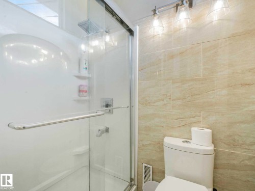 Glass-enclosed shower with a showerhead and two built-in shelves, complemented by light-toned wall tiling and a three-light vanity fixture - 9207 169 Street, Edmonton, AB - Indoor Photo Showing Bathroom