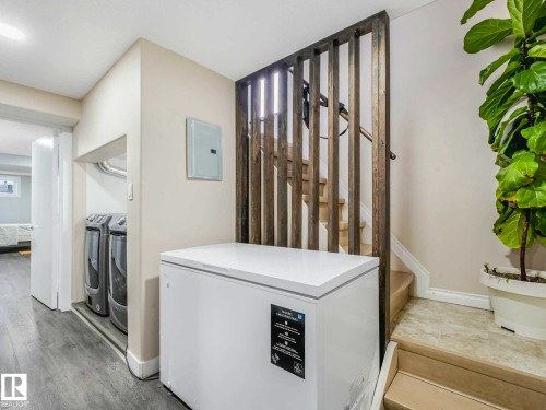Modern laundry area featuring a washer and dryer, wood-finish flooring, and a contemporary wood slat room divider - 9207 169 Street, Edmonton, AB - Indoor Photo Showing Laundry Room