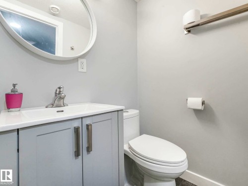 Contemporary bathroom featuring a white oval mirror, single basin vanity with a light gray cabinet and brushed nickel hardware, and a white toilet - 9207 169 Street, Edmonton, AB - Indoor Photo Showing Bathroom
