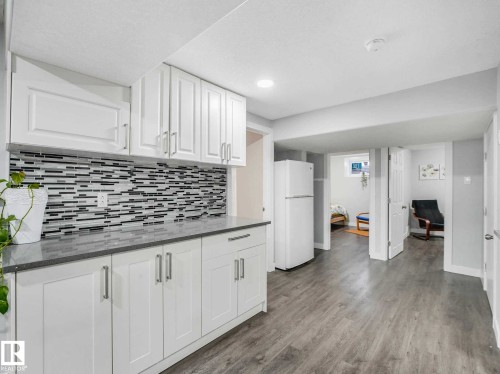 Kitchenette featuring white cabinetry, a mosaic tile backsplash, grey countertops, and wood-finish flooring - 9207 169 Street, Edmonton, AB - Indoor Photo Showing Kitchen