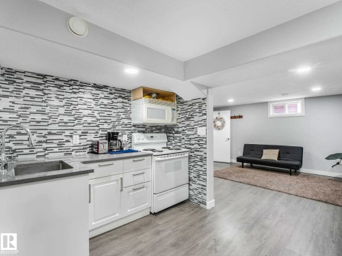 Kitchenette featuring white cabinetry with brushed chrome hardware, a stainless steel sink with a high-arc faucet, and a light-toned countertop - 9207 169 Street, Edmonton, AB - Indoor Photo Showing Kitchen