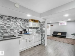 Kitchenette featuring white cabinetry with brushed chrome hardware, a stainless steel sink with a high-arc faucet, and a light-toned countertop - 