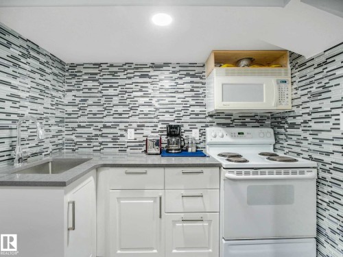 Compact kitchen featuring a mosaic tile backsplash and overhead microwave - 9207 169 Street, Edmonton, AB - Indoor Photo Showing Kitchen