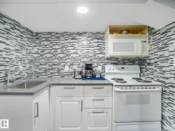 Compact kitchen featuring a mosaic tile backsplash and overhead microwave - 