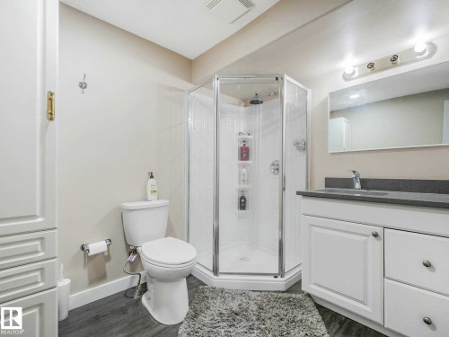 Bathroom featuring a glass-enclosed corner shower, single vanity with a gray countertop, wood-finish flooring, and white cabinetry - 9207 169 Street, Edmonton, AB - Indoor Photo Showing Bathroom