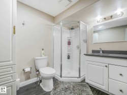 Bathroom featuring a glass-enclosed corner shower, single vanity with a gray countertop, wood-finish flooring, and white cabinetry - 