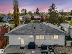 Rear exterior featuring a spacious wooden deck with stone landscaping, white siding, and a shingled roof - 