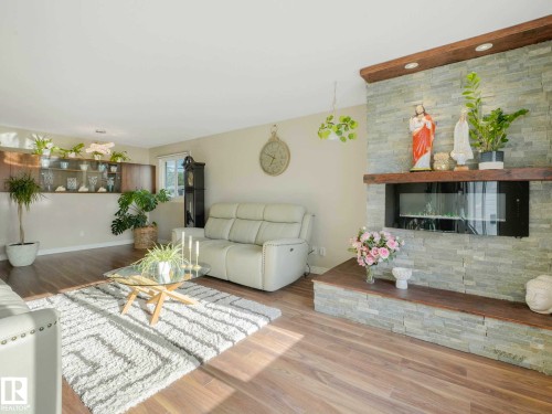 Living area featuring wood-finish flooring, a stacked stone fireplace with a wood mantle, and an integrated linear electric insert - 9207 169 Street, Edmonton, AB - Indoor Photo Showing Living Room With Fireplace