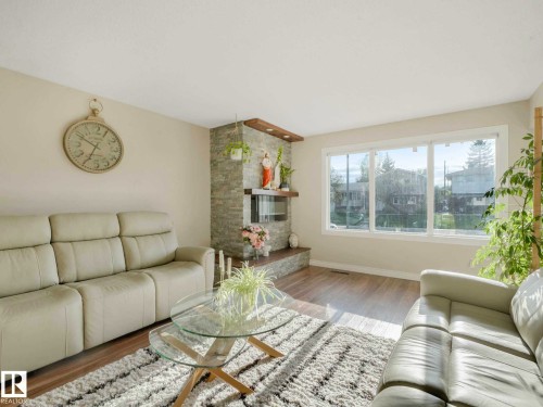 Living area featuring light wood-finish flooring, a stone-clad fireplace with wood mantle, and a large multi-pane window - 9207 169 Street, Edmonton, AB - Indoor Photo Showing Living Room