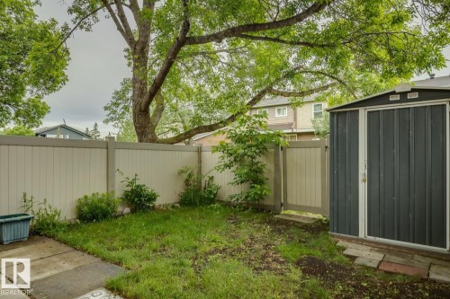 Enclosed backyard featuring a privacy fence, a detached storage shed, a mature tree, and a paved patio area - 1131 Hooke Road, Edmonton, AB 