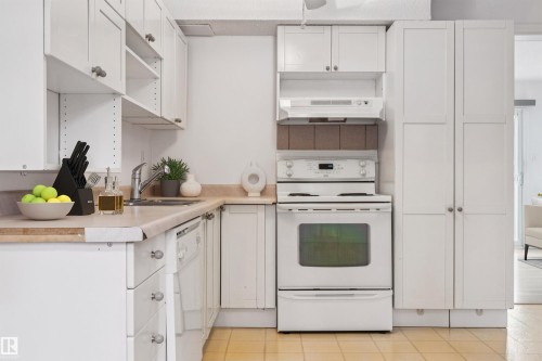 Kitchen featuring white cabinetry, beige countertops, a built-in sink, a white electric range with a range hood, and light-colored tile flooring - 1131 Hooke Road, Edmonton, AB 