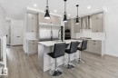 Modern kitchen featuring a central island with countertop seating, stainless steel appliances, and wood-finish flooring - 3234 Chernowski Way, Edmonton, AB 