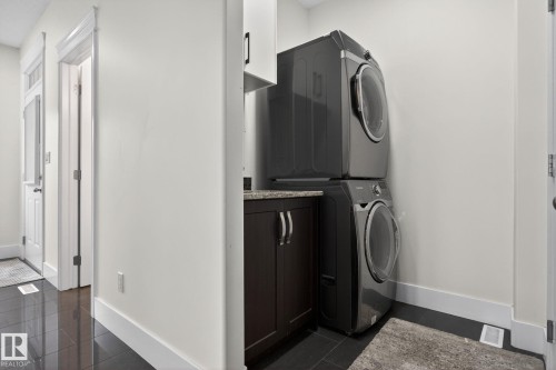 Dedicated laundry area featuring a stacked washer and dryer, dark wood-finish cabinetry, a stone-look countertop, and overhead white cabinetry - 9628 221 Street, Edmonton, AB 