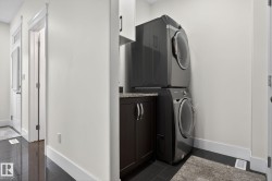 Dedicated laundry area featuring a stacked washer and dryer, dark wood-finish cabinetry, a stone-look countertop, and overhead white cabinetry - 