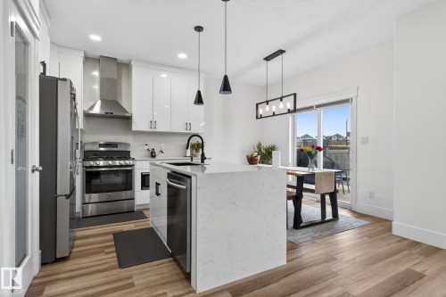 Modern kitchen featuring a large center island with integrated sink, stainless steel appliances, white cabinetry with contemporary hardware, and wood-finish flooring - 9628 221 Street, Edmonton, AB 