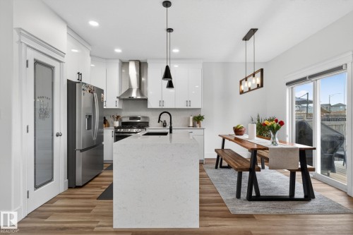 Open-concept kitchen featuring a large island with a sink, white cabinetry, stainless steel appliances, and wood-finish flooring - 9628 221 Street, Edmonton, AB 