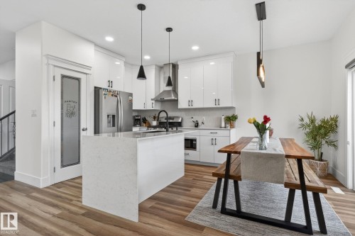 Modern kitchen featuring white cabinetry, a central island with a waterfall countertop, stainless steel appliances, and wood-finish flooring - 9628 221 Street, Edmonton, AB 