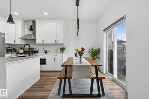 Modern kitchen featuring a waterfall island, white cabinetry, integrated stainless steel appliances, wood-finish flooring, and a sliding glass door - 9628 221 Street, Edmonton, AB 
