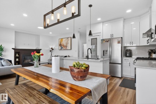 Open-concept kitchen and living area featuring wood-finish flooring, recessed lighting, and a modern linear chandelier - 9628 221 Street, Edmonton, AB 
