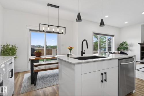 Open-concept kitchen and dining area featuring a white kitchen island with a black sink and faucet, integrated dishwasher, and pendant lighting - 9628 221 Street, Edmonton, AB 