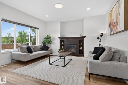 Living room featuring large windows, wood-finish flooring, recessed lighting, and a built-in fireplace with dark wood surround - 9628 221 Street, Edmonton, AB 