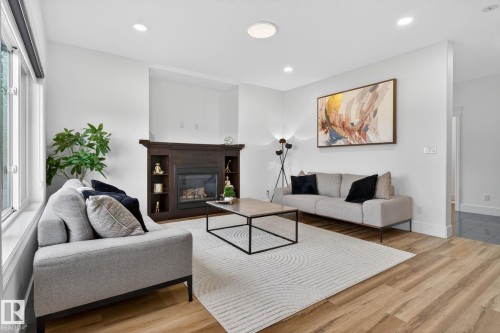 Living area featuring a dark wood-finish fireplace with built-in shelving, wood-finish flooring, recessed lighting, and large windows - 9628 221 Street, Edmonton, AB 