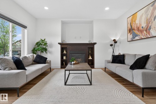 Living area featuring a dark wood fireplace with built-in shelving, recessed ceiling lighting, a large window, and wood-finish flooring - 9628 221 Street, Edmonton, AB 