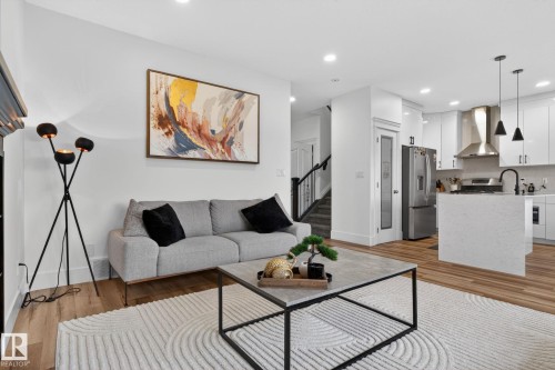Open-concept living area featuring wood-finish flooring, recessed lighting, a modern staircase with black railings, a kitchen island, and stainless steel appliances - 9628 221 Street, Edmonton, AB 