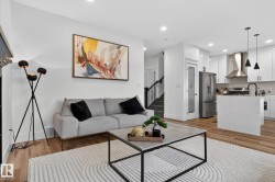 Open-concept living area featuring wood-finish flooring, recessed lighting, a modern staircase with black railings, a kitchen island, and stainless steel appliances - 