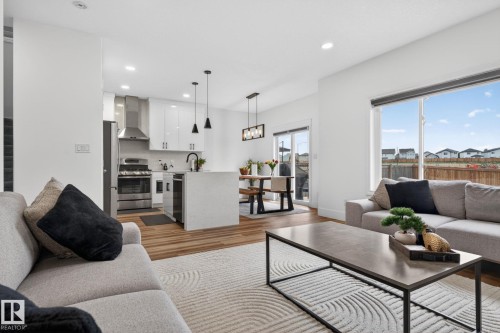 Open-concept living area featuring wood-finish flooring, a kitchen island with integrated beverage cooler, stainless steel appliances, and sliding glass doors to the exterior - 9628 221 Street, Edmonton, AB 