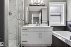 Bathroom featuring a white vanity with ample storage, a framed mirror, and a sleek light fixture - 