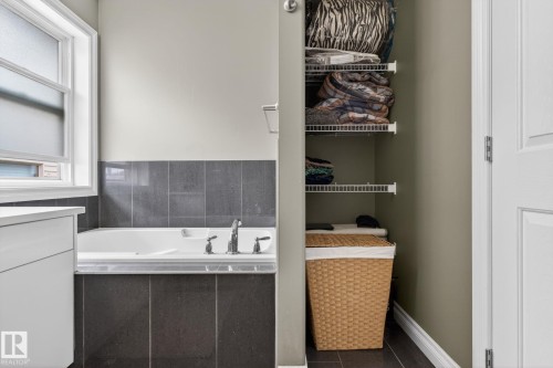 Built-in bathtub with dark tile surround, featuring chrome fixtures and a window with frosted glass - 9628 221 Street, Edmonton, AB 