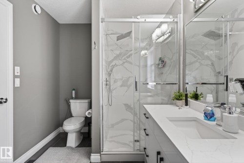 Modern bathroom featuring a glass-enclosed shower with marble-look wall tiling, a single vanity with an integrated rectangular sink, and dark wood-finish flooring - 9628 221 Street, Edmonton, AB 