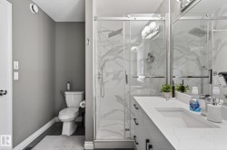 Modern bathroom featuring a glass-enclosed shower with marble-look wall tiling, a single vanity with an integrated rectangular sink, and dark wood-finish flooring - 