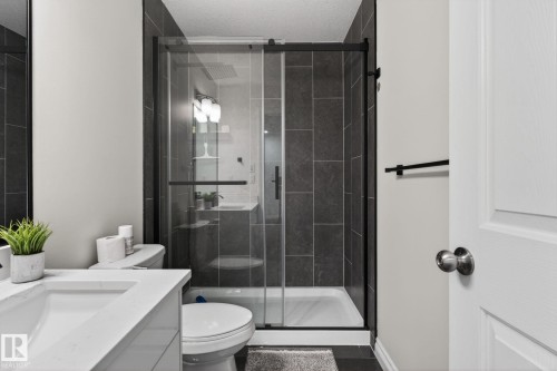 Contemporary bathroom featuring a glass-enclosed shower with dark tile surround, a sleek white toilet, and a vanity with an integrated sink and quartz-finish countertop - 9628 221 Street, Edmonton, AB 