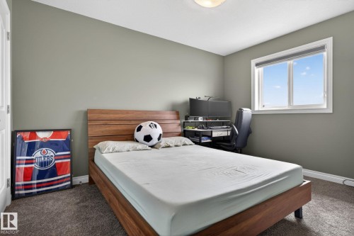 Carpeted room featuring a white-framed window, neutral painted walls, a wood-finish bed frame with an integrated headboard, and a white ceiling with a flush-mount light fixture - 9628 221 Street, Edmonton, AB 