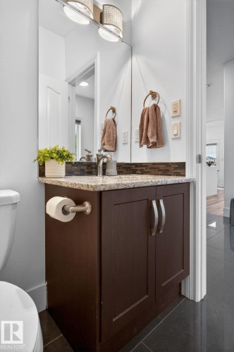 Powder room featuring a dark wood-finish vanity with a light-colored speckled countertop, a rectangular mirror, and a decorative two-light fixture - 9628 221 Street, Edmonton, AB 