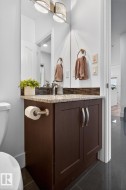 Powder room featuring a dark wood-finish vanity with a light-colored speckled countertop, a rectangular mirror, and a decorative two-light fixture - 