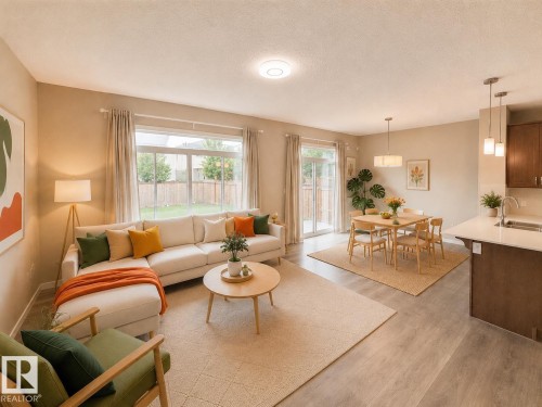 Open-concept living space featuring wood-finish flooring, a contemporary kitchen peninsula with light countertops, a dining area, a rear patio door, and large windows providing natural illumination - 22519 96 Avenue, Edmonton, AB 