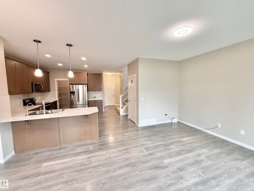Open-concept living space featuring wood-finish flooring, a kitchen island with integrated sink, stainless steel appliances, and ceiling-mounted lighting - 22519 96 Avenue, Edmonton, AB 