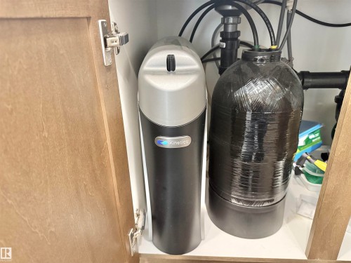 Under-sink water treatment system featuring a water softener and filtration unit, integrated within wood-finish cabinetry - 22519 96 Avenue, Edmonton, AB 