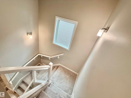 Staircase featuring light-toned carpet, a white handrail, and clear glass panel railings - 22519 96 Avenue, Edmonton, AB 